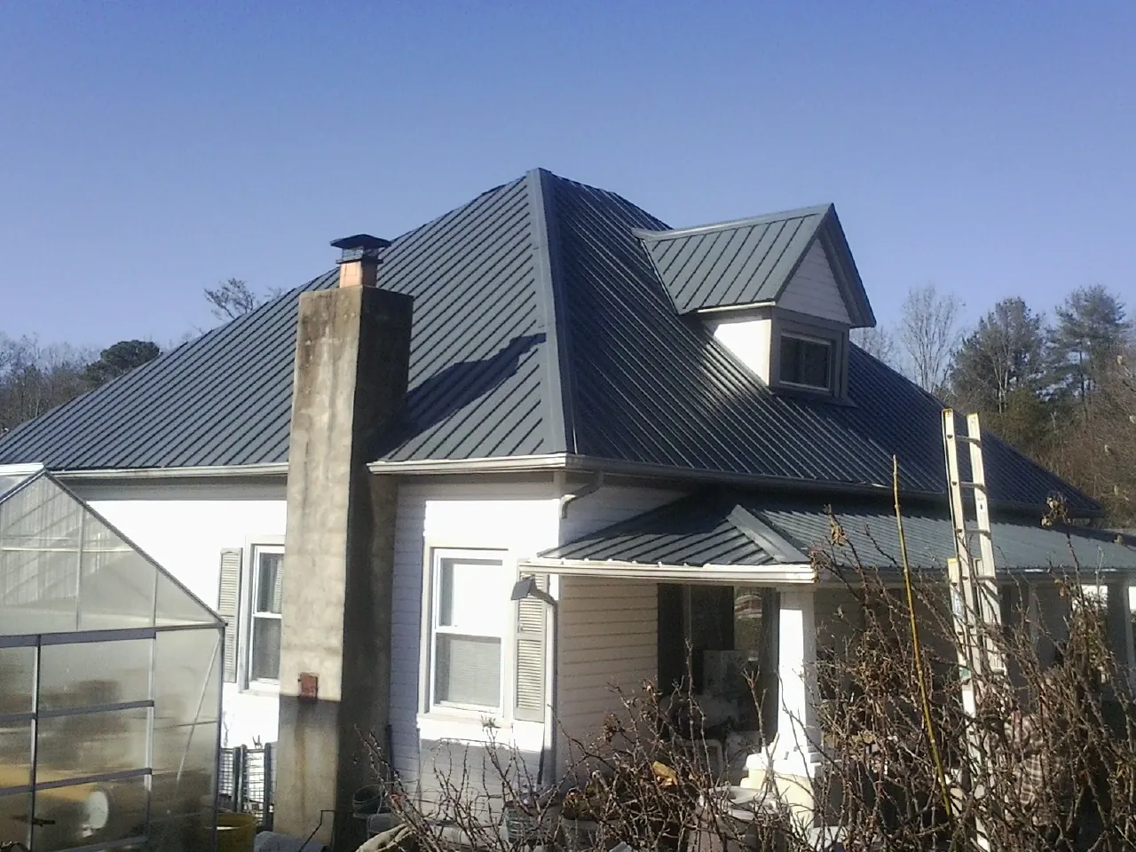 Dark blue standing seam metal roof on a white farmhouse with dormer — Slate & Tile Roof Repair by Roofing Brothers in Melcher Dallas