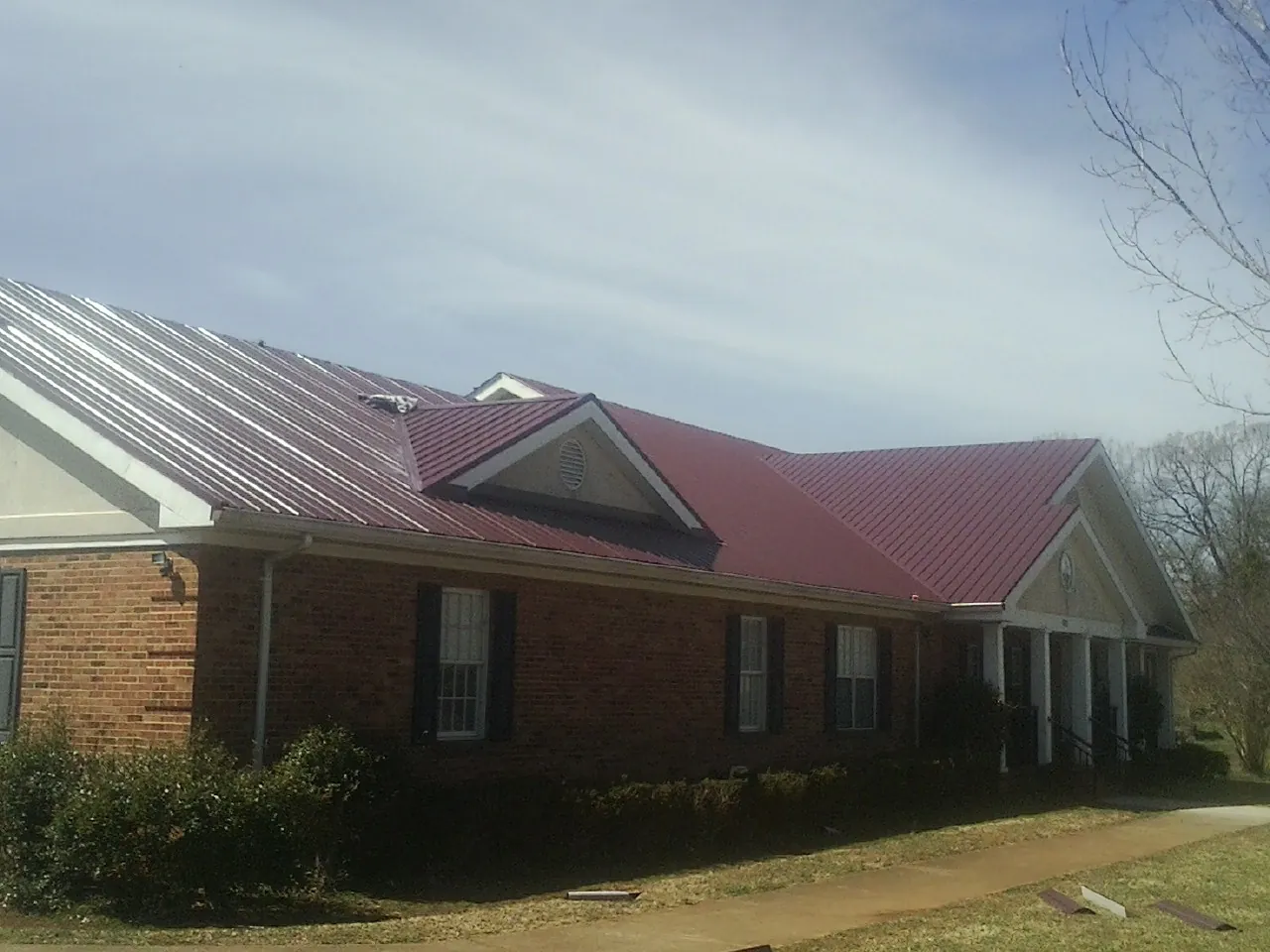 Red metal roof with gabled entries on a long brick building, from a Hail Damage Roof Repair job in Melcher Dallas