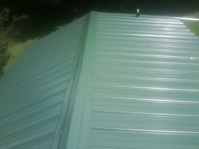 New green metal panels meeting at the ridge of a roof — Flat Roof Repair work by our crew in Melcher Dallas