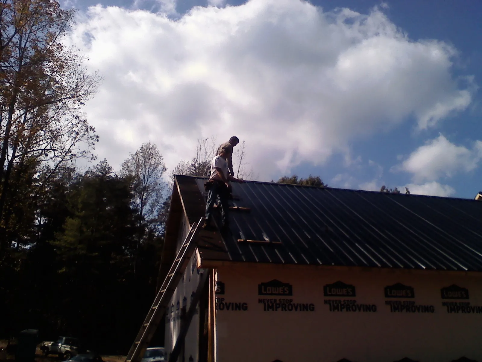 Roofer fastening dark metal panels high against a cloudy sky, from a Roof Inspection job in Melcher Dallas