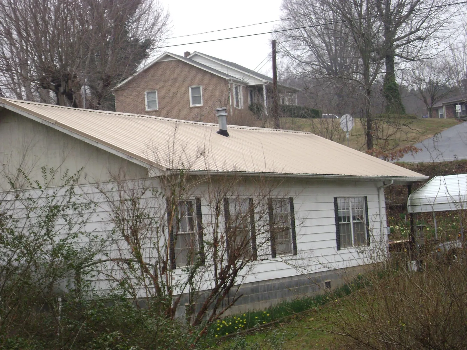 Tan metal roof on a white sided house set into a hillside — Commercial Roofing by Roofing Brothers in Melcher Dallas